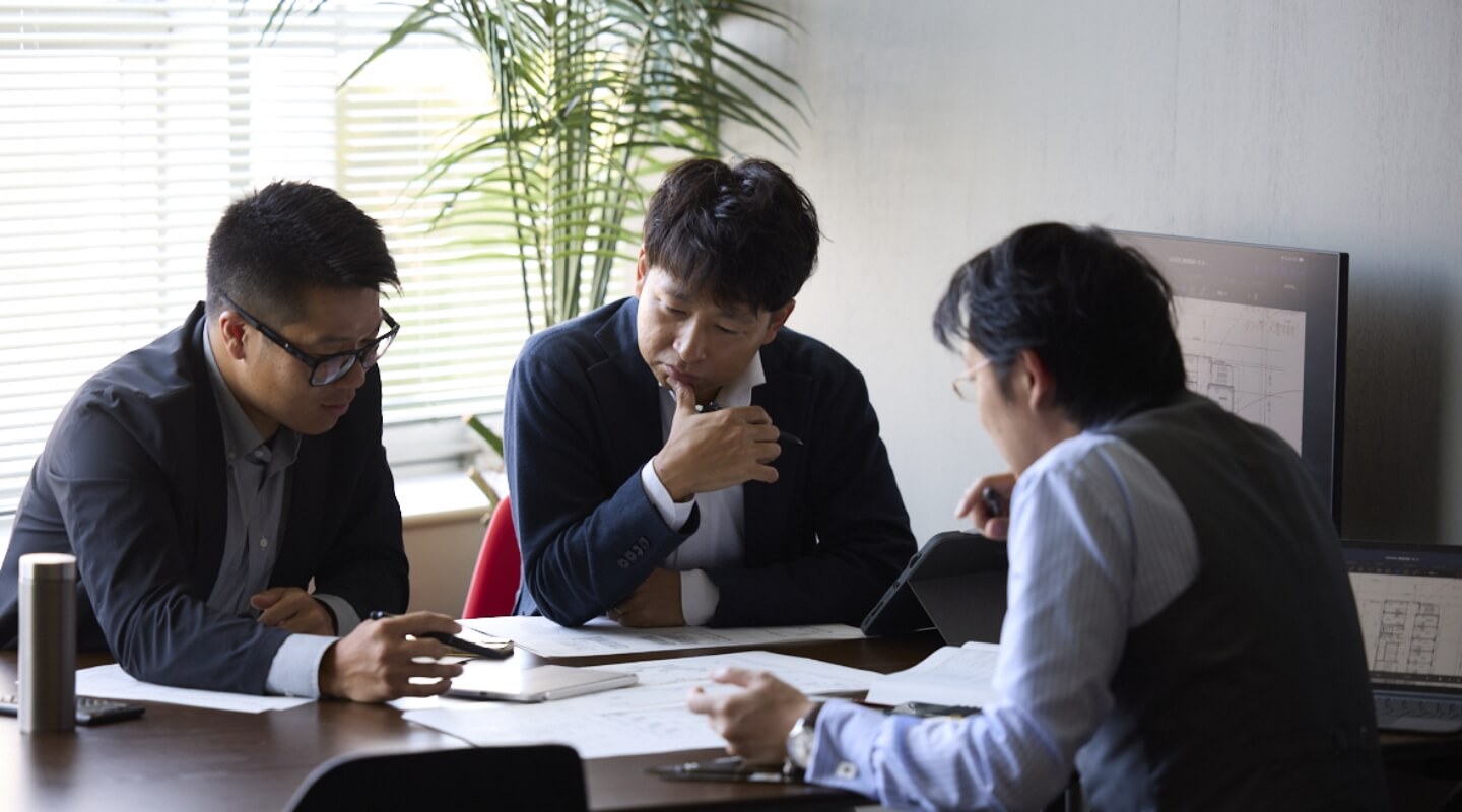 机に向かって話し合う3人の職員